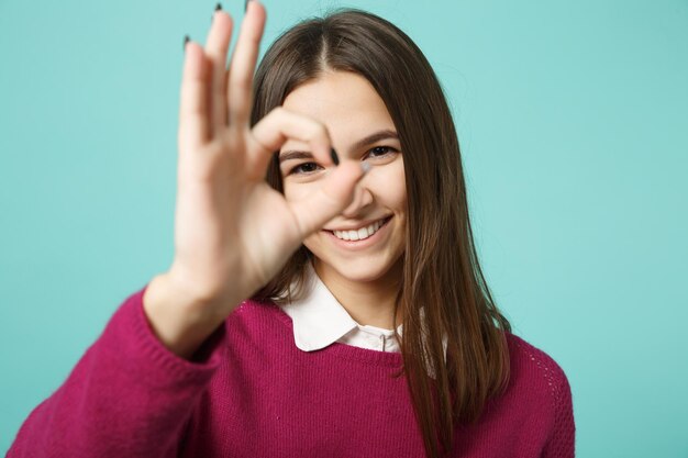 Young brunette woman girl in casual clothes posing isolated on blue wall background studio portrait. People emotions lifestyle concept. Mock up copy space. Close up showing OK gesture in front eye.