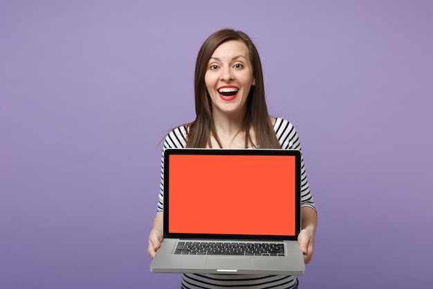 Young brunette woman girl in casual striped clothes posing isolated on violet purple background studio portrait. People sincere emotions lifestyle concept. Mock up copy space. Hold tablet pc computer.