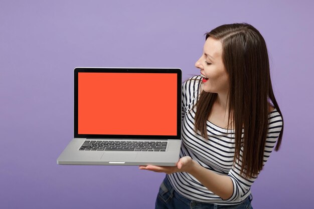 Young brunette woman girl in casual striped clothes posing isolated on violet purple background studio portrait. people sincere emotions lifestyle concept. mock up copy space. hold tablet pc computer