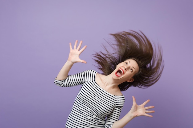 Young brunette woman girl in casual striped clothes posing isolated on violet purple wall background studio portrait. People sincere emotions lifestyle concept. Mock up copy space. Waving long hair.
