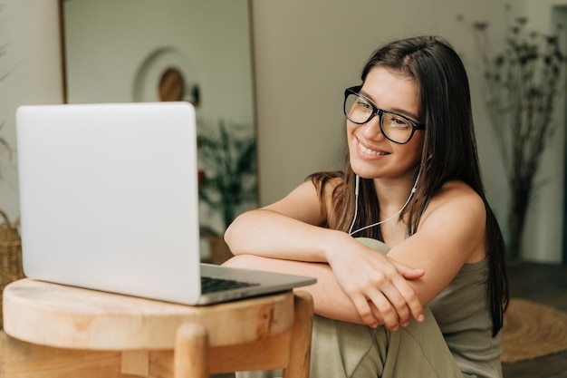 眼鏡をかぶった若い茶色の女性がラップトップとヘッドフォンを使ってビデオを見ています