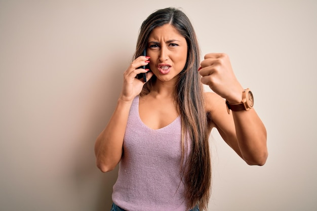 Young brunette woman having conversation talking on the smartphone over white background annoyed and frustrated shouting with anger crazy and yelling with raised hand anger concept