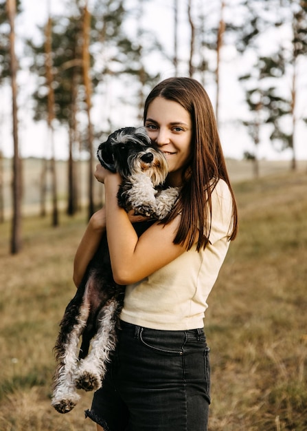 Young brunette woman holding in arms a miniature schnauzer breed dog smiling