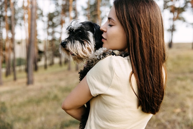 ミニチュア・シュナウザー犬を腕に抱いた若い茶色の女性