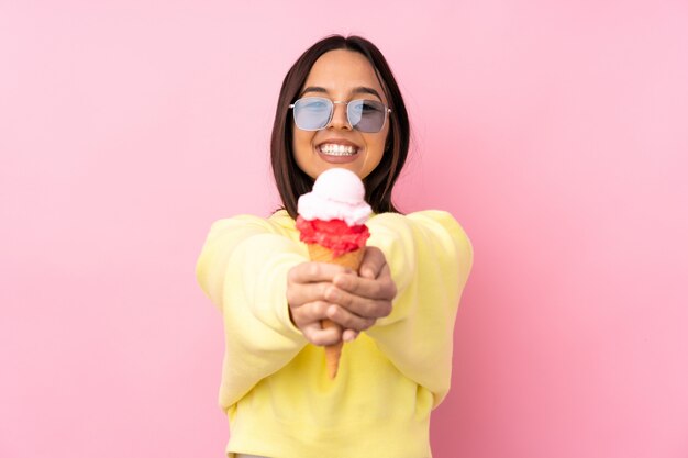 Young brunette woman holding a cornet ice cream over isolated pink wall holding copyspace imaginary on the palm to insert an ad