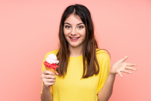 Young brunette woman holding a cornet ice cream over pink wall with shocked facial expression