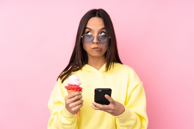 Young brunette woman holding a cornet ice cream thinking and sending a message