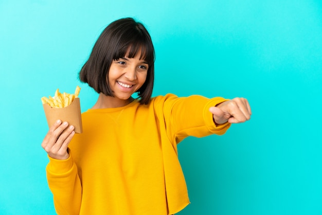 Молодая брюнетка женщина, держащая жареные чипсы на изолированном синем фоне, показывает палец вверх
