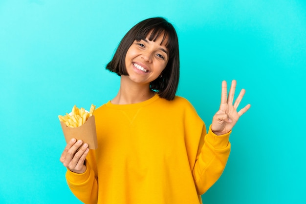 Giovane donna bruna che tiene patatine fritte su sfondo blu isolato felice e contando quattro con le dita