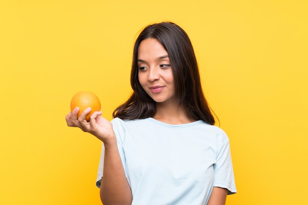 Young brunette woman holding an orange with happy expression