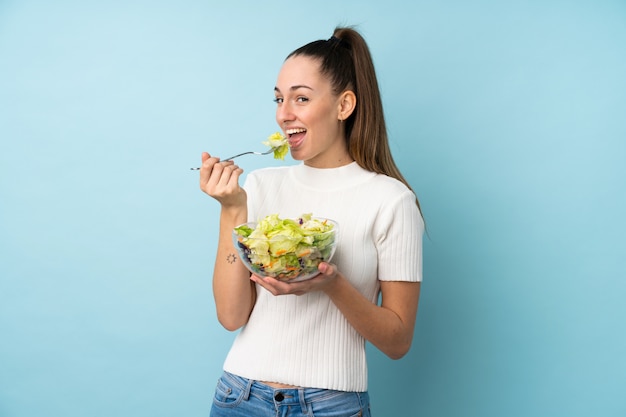 Young brunette woman holding a salad over isolated blue wall