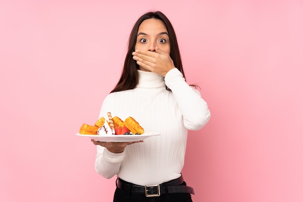 Young brunette woman holding waffles covering mouth with hands