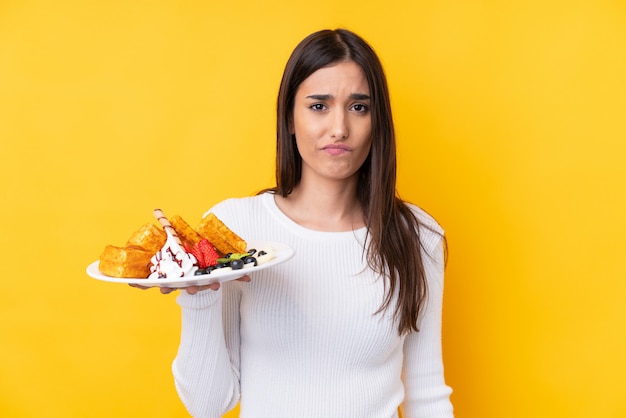 Young brunette woman holding waffles with sad expression