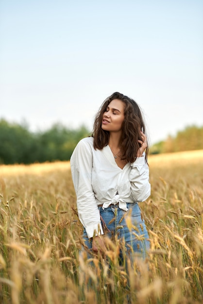写真 黄金の麦畑を背景に白いシャツとブルージーンズの若いブルネットの女性
