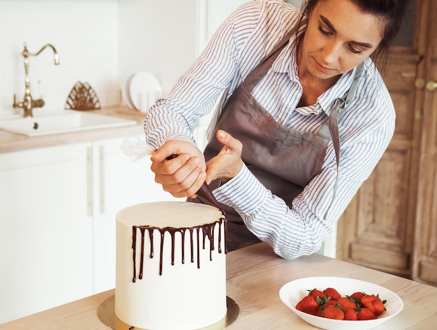 Foto giovane donna bruna è impegnata nella decorazione di una torta di piccole imprese domestiche