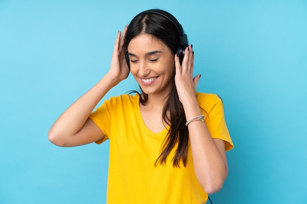 Young brunette woman over isolated blue wall listening music