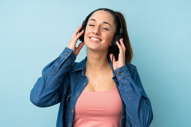 Young brunette woman over isolated blue wall listening music