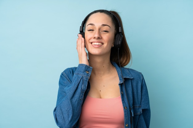 Young brunette woman over isolated blue wall listening music