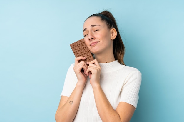 Молодая брюнетка женщина над синей стеной, принимая шоколадные таблетки и счастливым