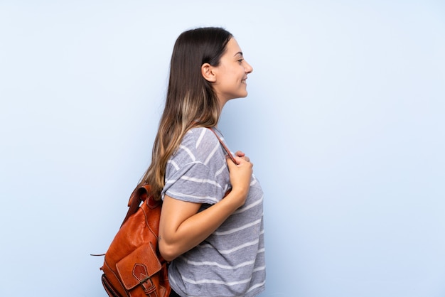 Young brunette woman isolated blue  with backpack