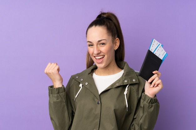 Young brunette woman over isolated purple wall happy in vacation with passport and plane tickets