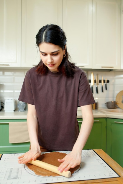 Young brunette woman knead the dough for shortcrust pastry on a baking mat vertical