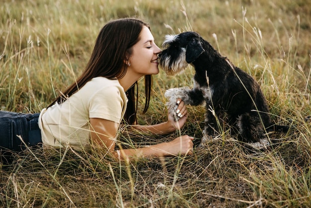 Young brunette woman lying in a field with a miniature schnauzer breed dog touching noses