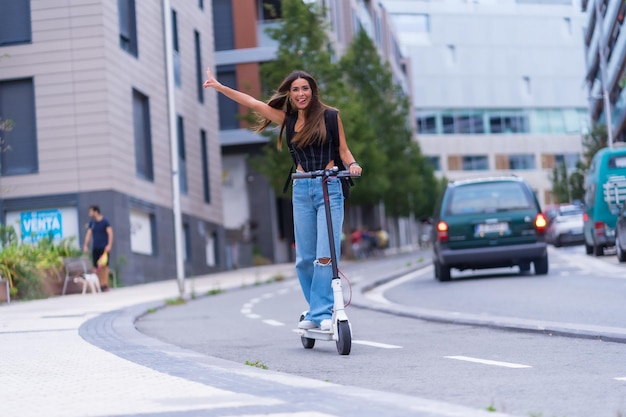 Una giovane donna bruna che si muove in città con uno scooter elettrico divertendosi lungo la pista ciclabile