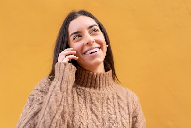 屋外で誰かと携帯電話で会話を続ける若いブルネットの女性