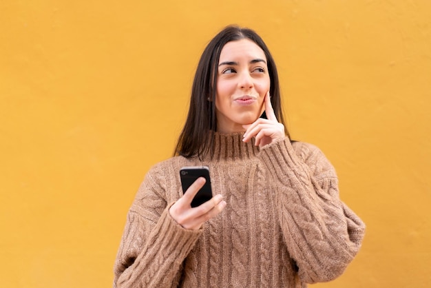 屋外で携帯電話を使用して考える若いブルネットの女性