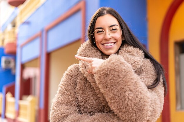 Young brunette woman at outdoors With glasses and pointing side