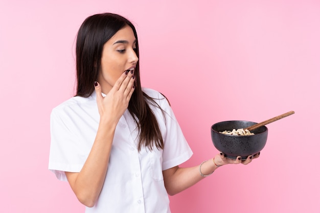 Young brunette woman over pink with surprise and shocked facial expression