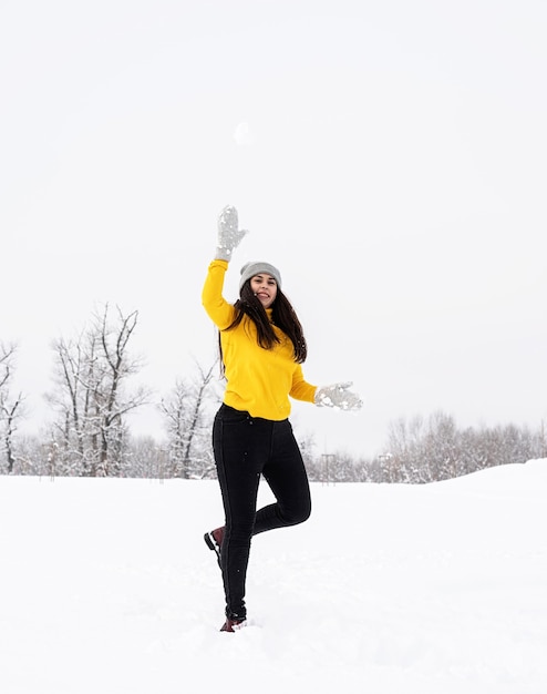 公園で雪と遊ぶ若いブルネットの女性