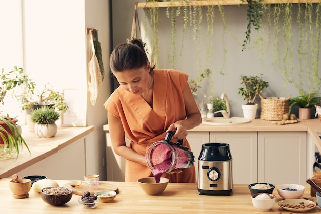young brunette woman pouring fresh smoothie into bowl