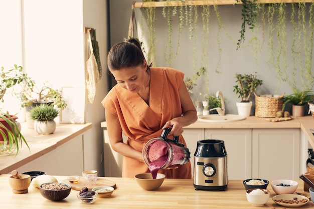 Young brunette woman pouring fresh smoothie into bowl