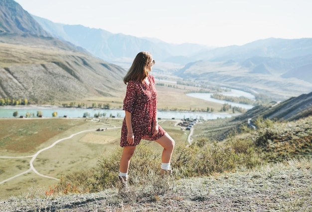 ターコイズブルーのカトゥニ川アルタイ山脈の背景に赤いドレスを着た若いブルネットの女性