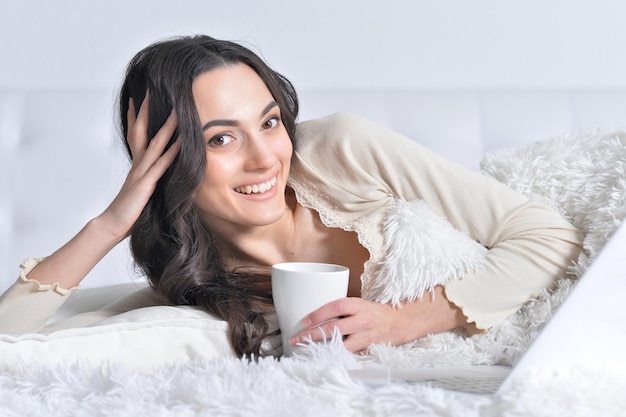 Young brunette woman relaxing in bed, using laptop