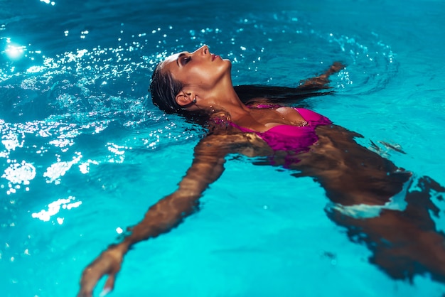 Giovane donna castana che si rilassa nella piscina.