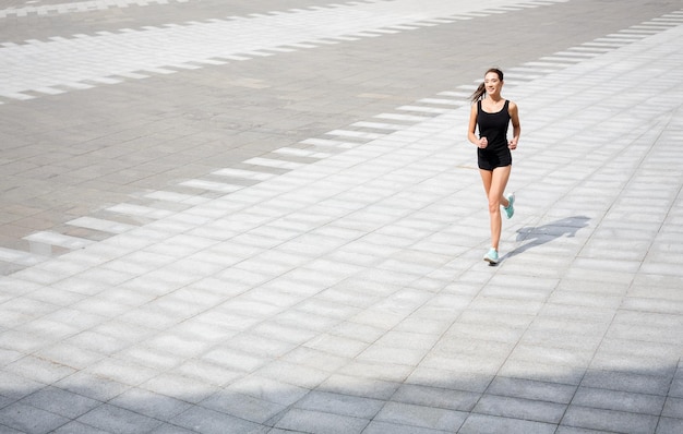 Young brunette woman running in city center, training before marathon, copy space