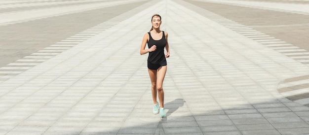 Young brunette woman running in city center, training before marathon, copy space