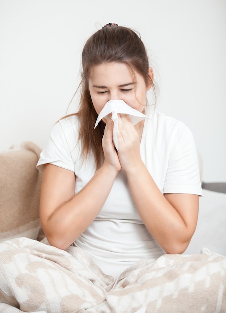 Young brunette woman sitting on bed and sneezing