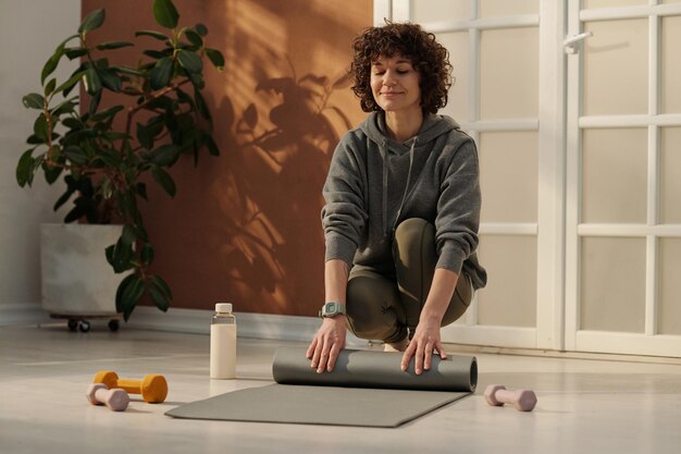 Young brunette woman in sportswear unrolling grey mat before workout