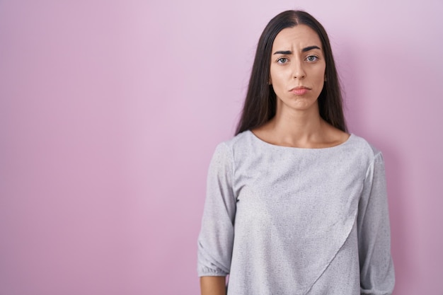 Young brunette woman standing over pink background depressed and worry for distress, crying angry and afraid. sad expression.