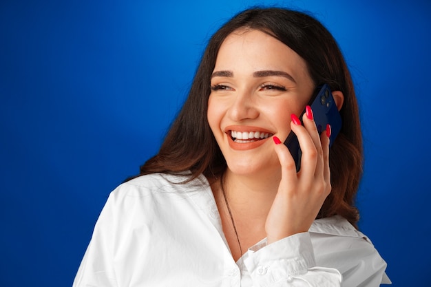 Young brunette woman talking on the phone against blue background