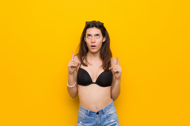 Photo young brunette woman wearing a bikini pointing upside with opened mouth