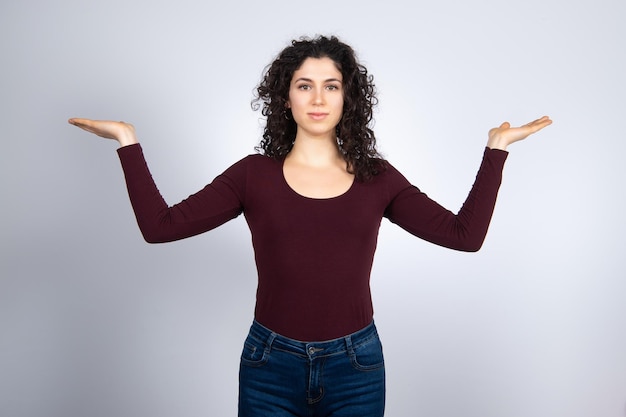 Young brunette woman wearing burgundy tshirt stretched hands to\
comparing pose caucasian girl imagining alternatives and weighing\
pros and cons isolated on white background making decisionxdxa