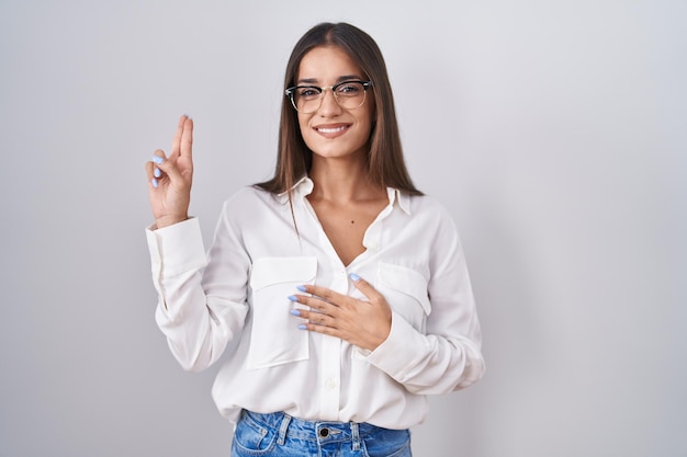 Young brunette woman wearing glasses smiling swearing with hand on chest and fingers up making a loyalty promise oath