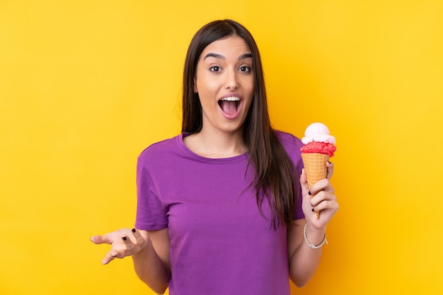 Young brunette woman with a cornet ice cream over isolated yellow wall with shocked facial expression