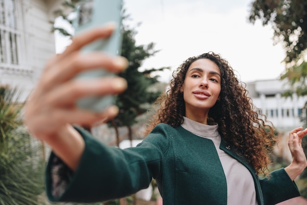 通りで写真を撮る巻き毛を持つ若いブルネットの女性