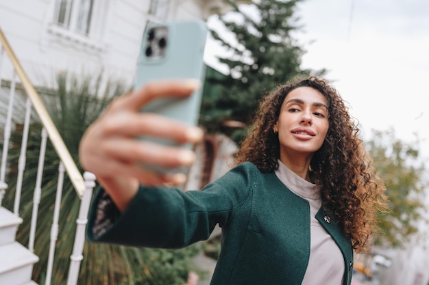 Young brunette woman with curly hair taking a photo over street
